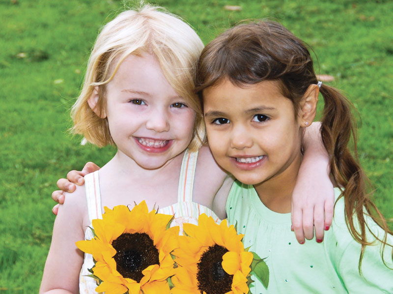 Two young girls holding sunflowers.